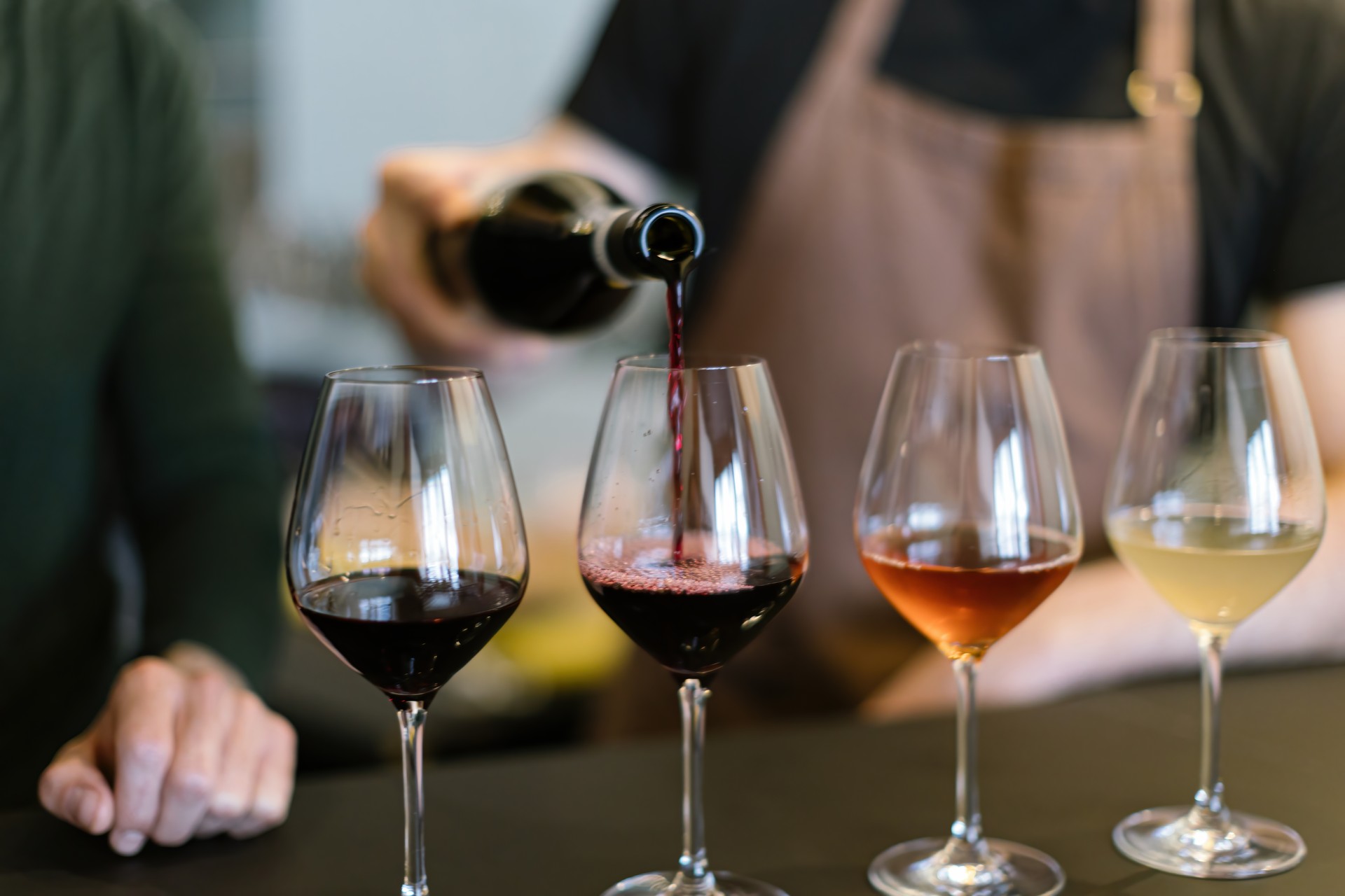 pouring different wines into the glasses arranged for the wine tasting on the counter