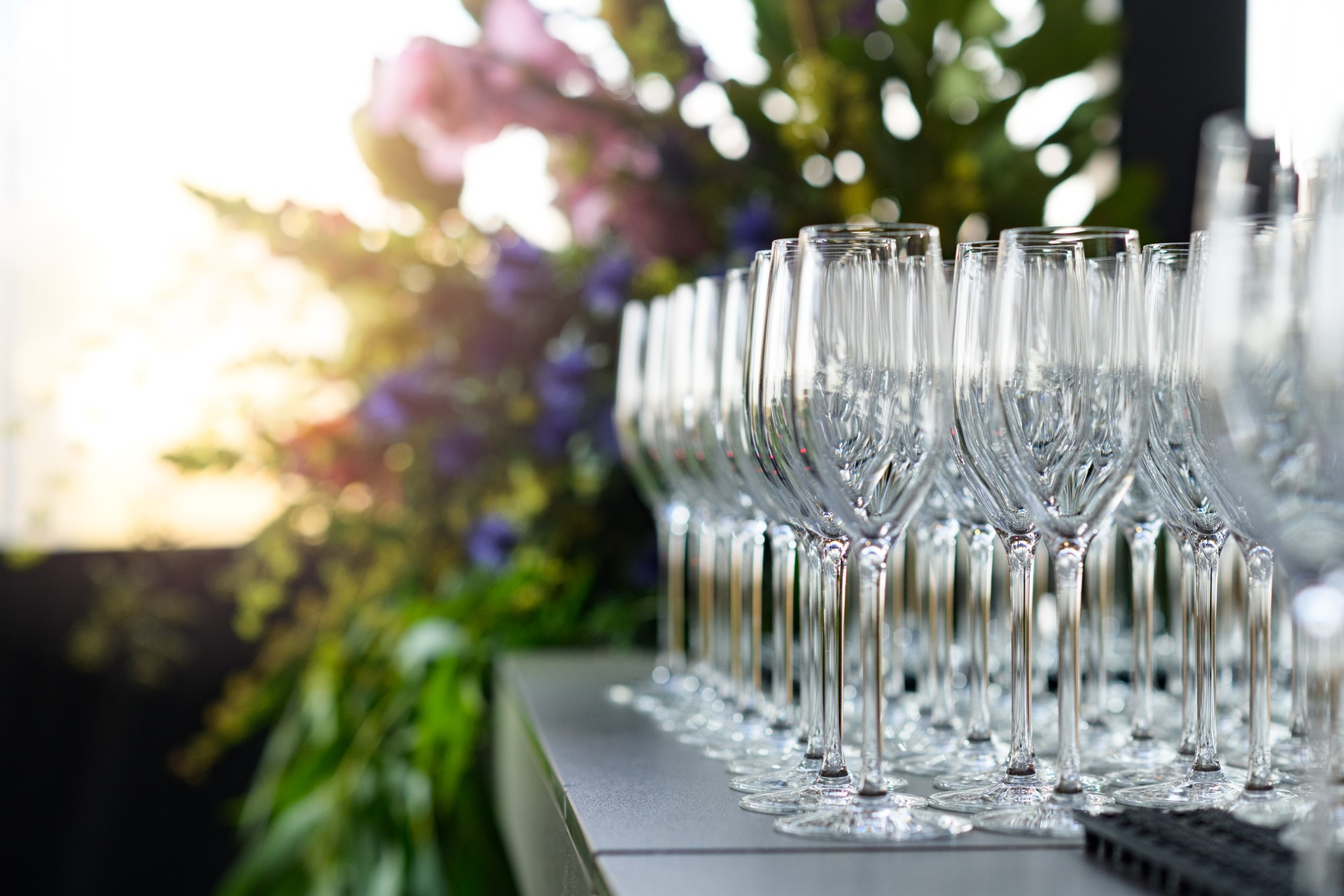 Rows of empty champagne flutes with defocussed flower arrangement at sunset